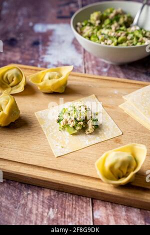 Faltanleitung von veganen Wontonknödeln mit Tofu und Brokkoli auf Holzschneidebrett, Seitenansicht Stockfoto