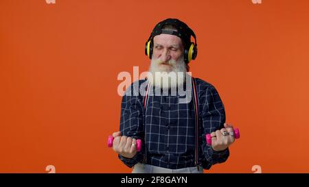 Älterer bärtiger Mann, der über Kopfhörer Musik hört, arbeitet, rosa Hanteln hebt, Gesundheitsfürsorge Stockfoto