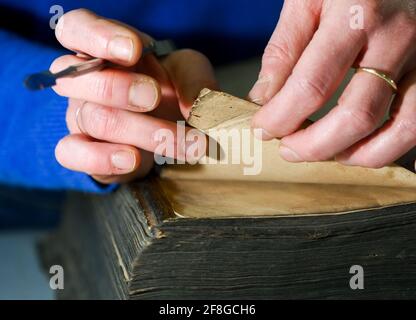 Berlin, Deutschland. April 2021. In der Papierwerkstatt Friedrichshagen wird eine bibel 'die ganze Heilige Schrift' aus dem Jahr 1737 repariert und unter anderem die Hundeohren entfernt. Im Geschäft von Frauke Grenz und Julia Flögel, eine Vielzahl von Schäden an Büchern, Briefen, Dokumenten, Karten, Reisekoffer, Boxen sowie Bilder werden repariert. Sie produzieren auch Bücher als Einzelstücke oder in kleineren Auflagen und bieten zahlreiche Kurse an. Quelle: Jens Kalaene/dpa-Zentralbild/ZB/dpa/Alamy Live News Stockfoto