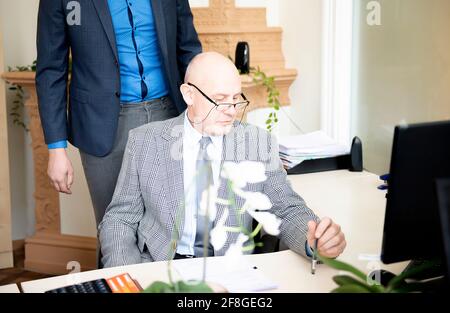 Schöner reifer Geschäftsmann im klassischen Anzug ist mit einem Computer Und einen Stift, während er in seinem Büro arbeitet Stockfoto