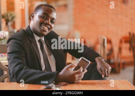 Afrikanischer Geschäftsmann mit Smartphone im Restaurant mit Lächeln und Glücklich Stockfoto