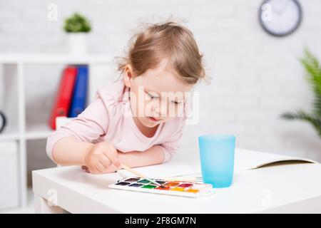 Kindheit, Bildung und Kreativität Konzept - nettes kleines Mädchen malen etwas mit Aquarellen Stockfoto