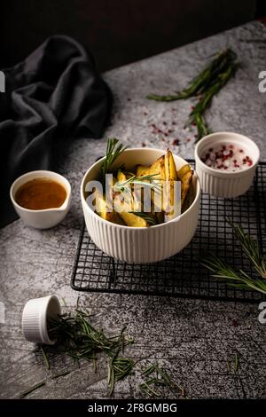 Rustikale Kartoffeln, in Scheiben geschnitten, mit Rosmarin. In einem weißen Gericht, mit Butter und Gewürzen auf dunklem Hintergrund. Menükonzept für Bar und Restaurant Stockfoto