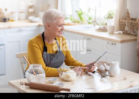 Glückliche alte Frau Kochen nach Rezepten aus dem Internet Stockfoto