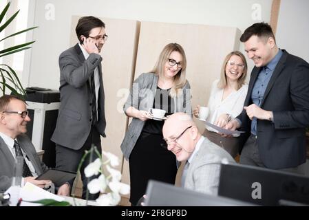 Geschäftsleute nutzen Gadgets, trinken Kaffee, reden und lachen, während sie im modernen Büro arbeiten Stockfoto