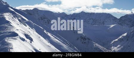 Malerische schneebedeckte Berge gegen blauen Himmel mit weißen Wolken während der Wintersaison in der Stadt Zakopane - Kasprowy Wierch . Schneebedeckte Gipfel berühren den bewölkten Himmel. Stockfoto