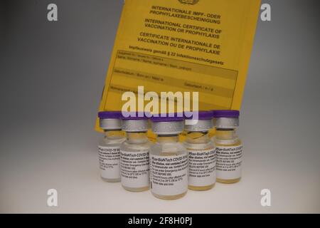 Original-Fläschchen mit Impfstoffen, angeordnet in einer Gruppe davor Von einem weißen Rückstand mit Impfpass hinter ihnen Stockfoto