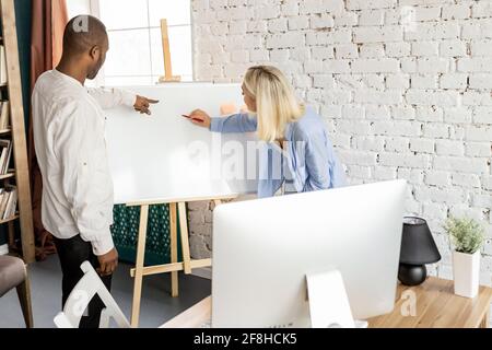 Seriöse, multirassische Kollegen arbeiten gemeinsam an einem Projekt im Büro und schreiben neue Ideen für das Startup auf dem Markerboard. Konzentriertes Geschäft Stockfoto