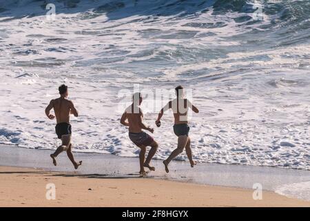 Männliche Urlauber, die sich in einem Aufenthalturlaub am Fistral Beach in Newquay in Cornwall ins Meer blicken lassen. Stockfoto