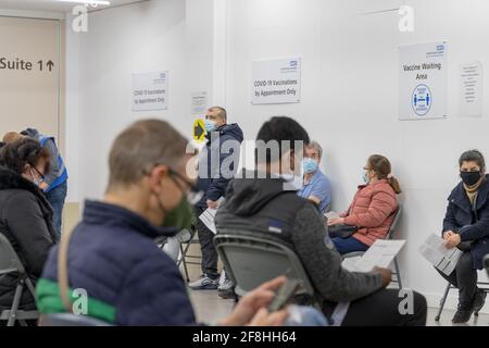 Männer und Frauen mit Gesichtsmasken mit Terminen für NHS-COVID-19-Impfungen warten im ausgewiesenen Wartebereich einer Klinik im Südosten Londons im Vereinigten Königreich Stockfoto