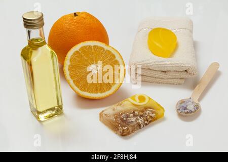 Schneiden Sie Orange mit einem ganzen Stück, einem Frottee-Handtuch, einer Flasche mit Aromatherapieöl, hausgemachter Seife und einem Holzlöffel mit Meersalz auf weißem Grund. Sp Stockfoto