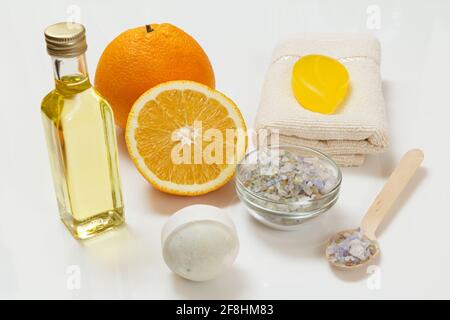 Schneiden Sie Orange mit einem ganzen Stück, einem Frottee-Handtuch, einer Flasche mit Aromatherapieöl, Seife, einer Badebombe und einem Holzlöffel mit Meersalz auf weißem Grund Stockfoto