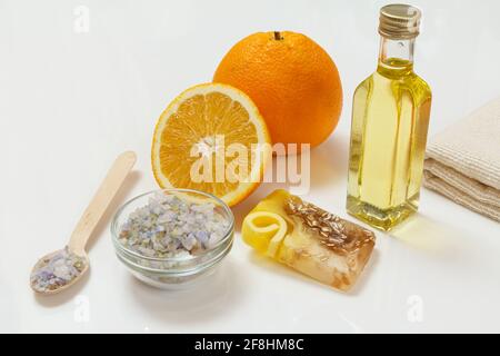 Schneiden Sie Orange mit einem ganzen Stück, einem Frottee-Handtuch, einer Flasche mit Aromatherapieöl, hausgemachter Seife und einem Holzlöffel mit Meersalz auf weißem Grund. Sp Stockfoto