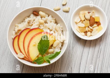 Sorghum Porridge mit Pfirsich-, Cashewnüssen und Mandel-Stücken in Porzellanschalen auf grauen Holzbrettern. Veganer glutenfreier Sorghum-Salat mit Früchten. Stockfoto