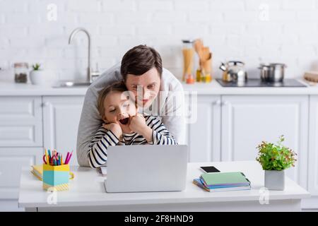 Aufgeregter Vater und Tochter, die sich während des Online-Unterrichts einen Laptop angeschaut haben Stockfoto