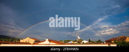 Panoramaaufnahme eines Regenbogens im wolkigen Himmel darüber Gebäude Stockfoto