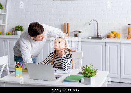 Vater und Tochter schauen sich während des Online-Unterrichts an In der Küche Stockfoto