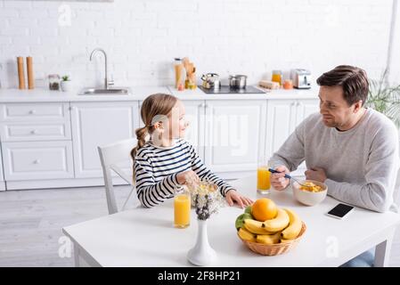 Fröhlicher Mann und Tochter, die sich beim Frühstück angucken In der Küche Stockfoto