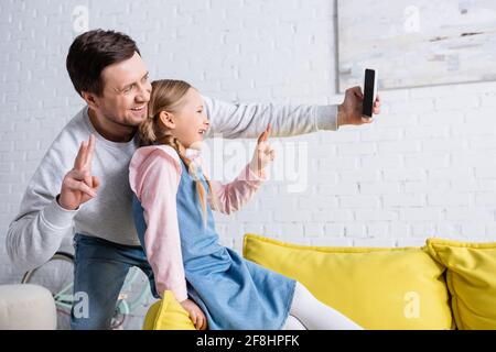 Fröhlicher Vater und Tochter zeigen beim Selfie eine Siegesgeste Auf dem Smartphone Stockfoto