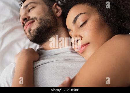 Nahaufnahme einer lockigen afroamerikanischen Frau, die den bärtigen Mann umarmt Und im Schlafzimmer liegen Stockfoto