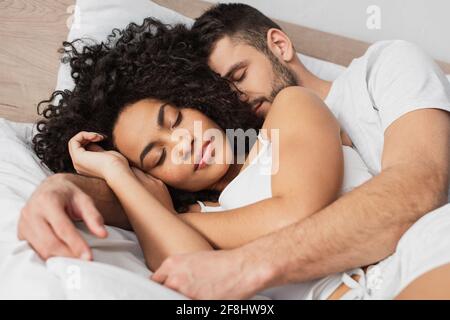 Multiethnischer Mann und Frau umarmen sich, während sie im Bett schlafen Stockfoto