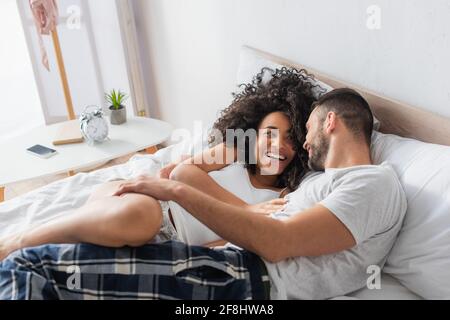 Fröhliches interrassisches Paar, lächelnd und auf dem Bett liegend Stockfoto