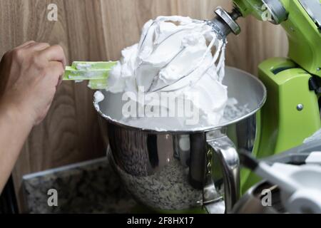 Hand einer Frau mit Spachtel, die Schlagsahne aus Küchenarmatur in eine Schüssel nimmt. Gerät zum Nachtisch Stockfoto