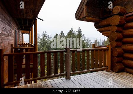 Blick auf die Spitze der Bäume von einem großen Balkon in einer Blockhütte und Schneefall Stockfoto