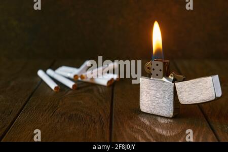 Vintage-Feuerzeug aus Metall mit Flamme und Zigaretten auf dunklem Hintergrund, Nahaufnahme Stockfoto