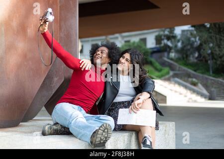 Junges multiethnisches Paar, das zusammen mit einer analogen Kamera ein lächelndes Foto gemacht hat. Sie befinden sich im Freien. Platz für Text. Stockfoto