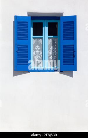 Typische lokale Architektur der Kykladen-Inseln, Griechenland, weiß getünchte Wände und blaue Fenster, gelegentlich mit Stickereien als Vorhänge. Stockfoto