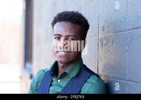 Ein hübscher lächelnder junger schwarzer Mann lehnt sich an einen Grauen Betonblockwand Stockfoto