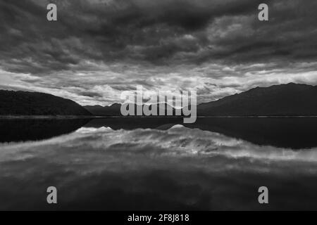 Schwarz-Weiß-Foto von Bergen und Sturmwolken, die sich im Lake Burbury in Tasmanien, Australien, am Rande von Tasmaniens Welterbe Wildern spiegeln Stockfoto