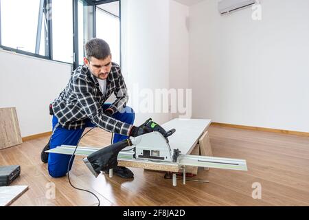 Ein Zimmermann schneidet eine Holzdiele der Arbeitsfläche auf dem Boden des Raumes. Er führt seine Arbeitsaufgabe auf einer Holzkiste aus, die ihm als Werk diente Stockfoto