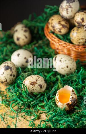 Draufsicht auf Korb mit Wachteleiern auf grünem Gras und rustikalem Holztisch, selektiver Fokus, schwarzer Hintergrund, vertikal Stockfoto