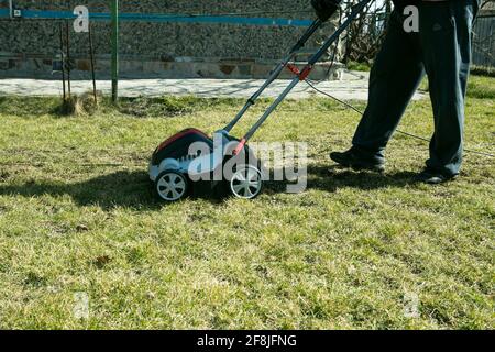 Belüftung mit einem Vertikutierer. Mit einem Scarifier im Garten zur Verbesserung der Rasenqualität im Frühjahr. Ein Arbeiter, Gärtner Betrieb Bodenbelüftung Stockfoto