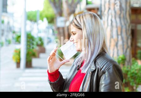 Glückliche kaukasische Frau, die nach der Wiedereröffnung auf der Straße spazierend ist, zeigt ein schönes toothy smile.Young girl tragend Schutzmaske Walking. Stockfoto