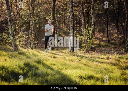 Mann in Mütze und dunklem Trainingsanzug, der durch den Wald läuft Stockfoto