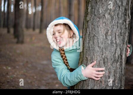 Teen Mädchen Blick aus hinter dem Baum in der Wald und Lachen Stockfoto