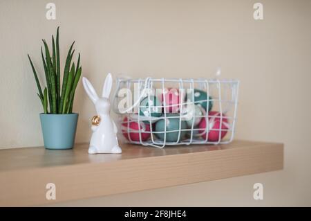 Osterhase aus Keramik mit einem goldenen Ei im Arm und Eiern im Korb. Stockfoto