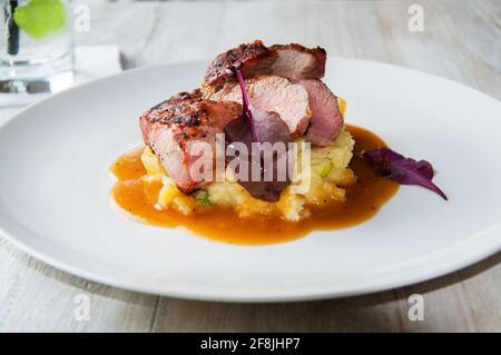 Schweinefilet mit Birnensauce und Kartoffelpüree auf weißem Teller auf weißem Tisch, trinken. Stockfoto