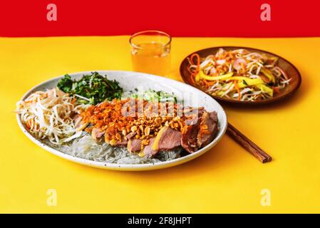 Portion geröstete Ente mit Glasnudel, bestreut mit gerösteten Zwiebeln und gehackten Nüssen mit Kräuter- und Gemüsesalat, Essstäbchen, Glas mit Essig Stockfoto