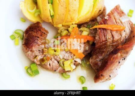 Schweinefilet mit Gemüse und gekochter Schnittkartoffel auf weißem Teller auf hellem Holztisch. Stockfoto