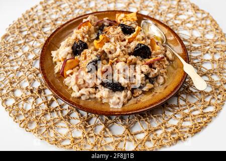 Traditioneller Haferbrei mit Apfelstücken, getrockneten Pflaumen und Honig auf dem Teller mit Löffel auf Bambus-Tischset. Gesundes Frühstück, Snack oder Hauptmahlzeit. Stockfoto