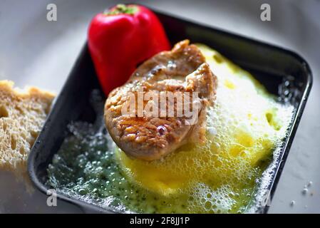 Kleines Rindersteak Braten auf heißem Käse und rotem Pfeffer auf Raclette Pfanne Grill, Nahaufnahme. Stockfoto