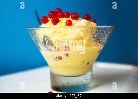 Taugglas-Becher mit Vanilleeis und roter Johannisbeere auf weißem und blauem Hintergrund, Nahaufnahme. Stockfoto