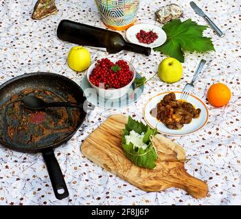 Brunch, Mittag- oder Abendessen im Freien. Mahlzeiten auf Tischtuch. Früchte, (Apfel, Orange, Johannisbeere, geröstete Leber, schmutzige Pfanne, Weinblatt und Flasche, Reis im Blatt. Stockfoto