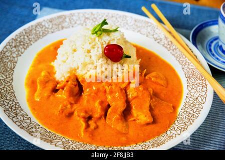 Hühnerfleisch in würziger Mangosauce und Reis auf weißem Teller mit Essstäbchen auf blauem Hintergrund, Nahaufnahme. Asiatisches Essen. Stockfoto