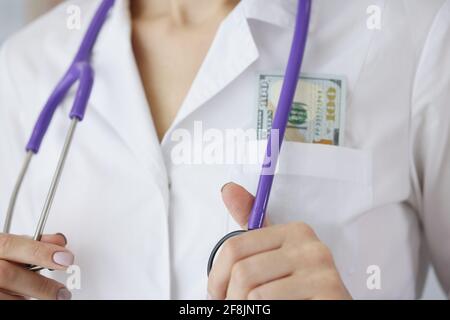 Arzt mit Dollarscheinen in der Tasche, der Stethoskop in der Nähe hält Stockfoto