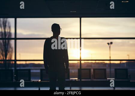 Nachdenklicher Passagier, der auf das Flugzeug wartet. Silhouette eines Mannes am Flughafen bei Sonnenaufgang. Stockfoto